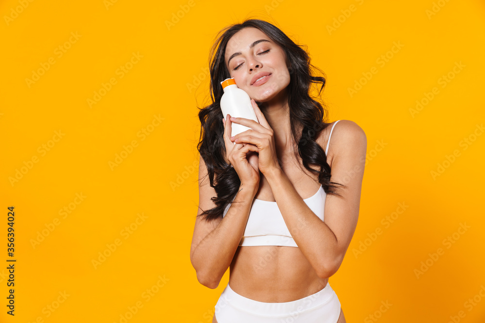 Image of pleased brunette cute woman in swimsuit holding sunscreen Image of pleased brunette cute woman in swimsuit holding sunscreen
