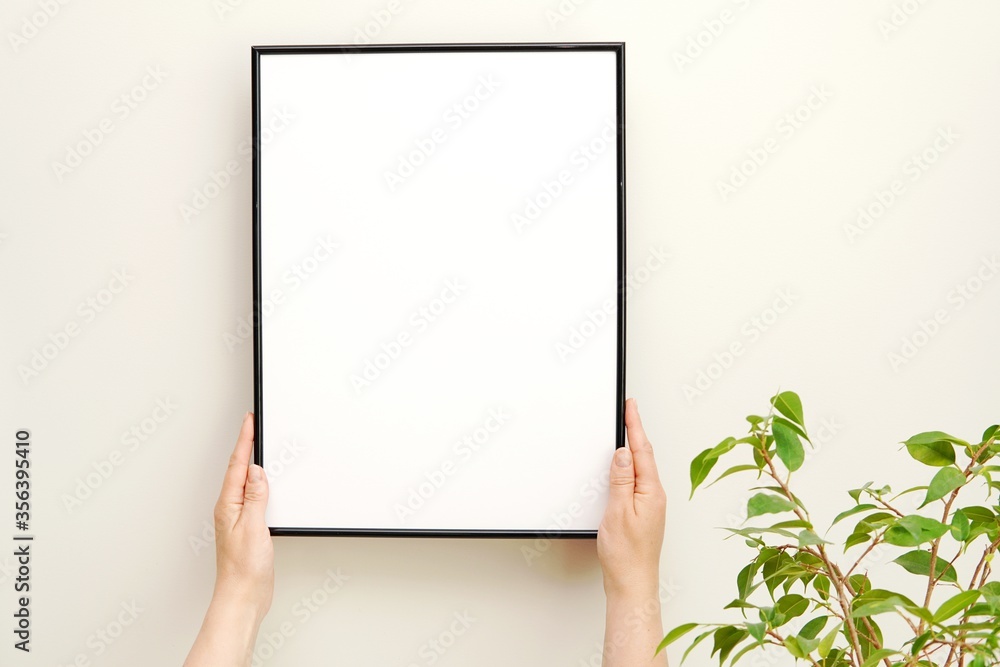 Styled stock photo, blank black frame mockup and greenery, hands holding frame, minimalist interior, green plant, artwork display. Styled stock photo, blank black frame mockup and greenery, hands holding frame, minimalist interior, green plant, artwork display.