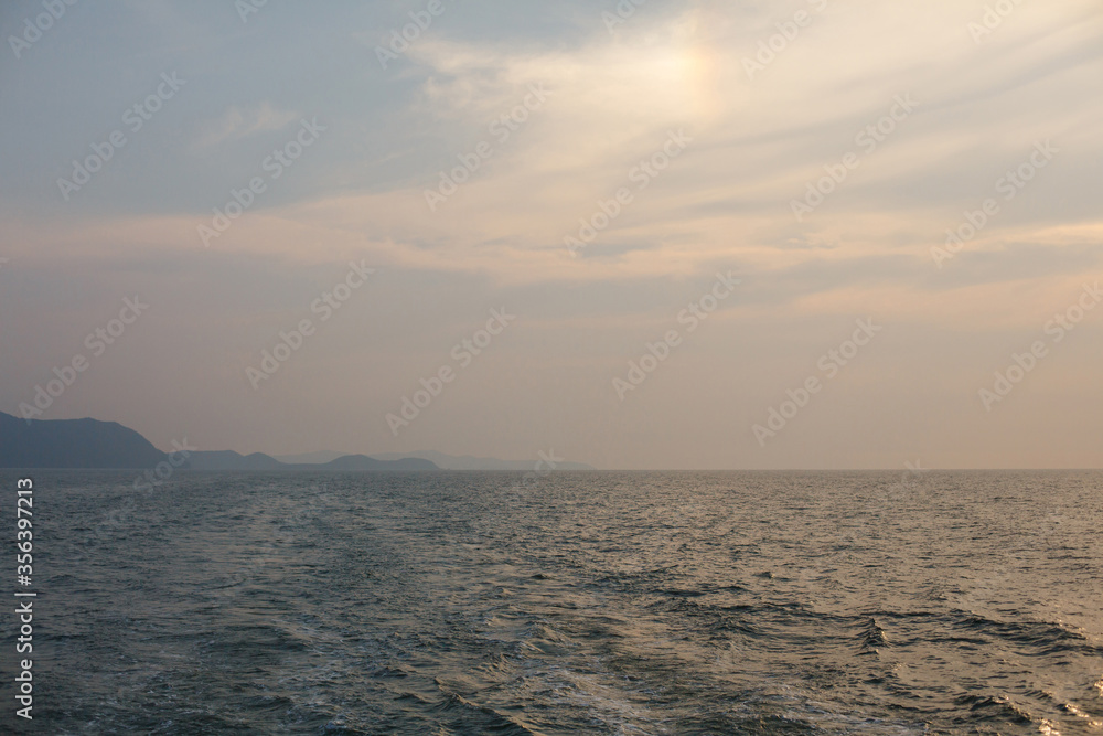 Natural background. Blue sea waves and foam at sunset day. Sunset over the water. Shore and land on the horizon