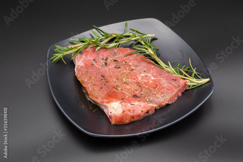 Raw beef with rosemary in black dish on black background, copyspace for you design.