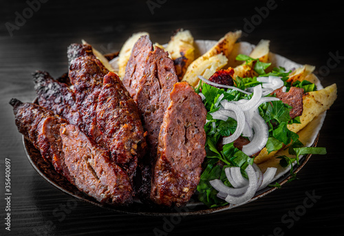 cut Lulia kebab with potato in plate on black wooden table background photo