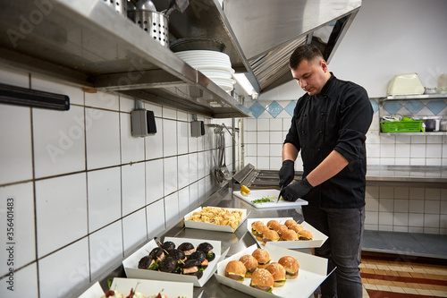 Young chef cook in black tunic prepares catering snacks.