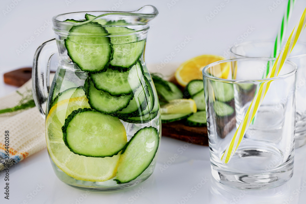 Cold drink made of cucumber and lemons, homemade lemonade in a decanter and two empty glasses, on a white background, shallow depth of field, selective focus. Healthy drinks concept Cold drink made of cucumber and lemons, homemade lemonade in a decanter and two empty glasses, on a white background, shallow depth of field, selective focus. Healthy drinks concept