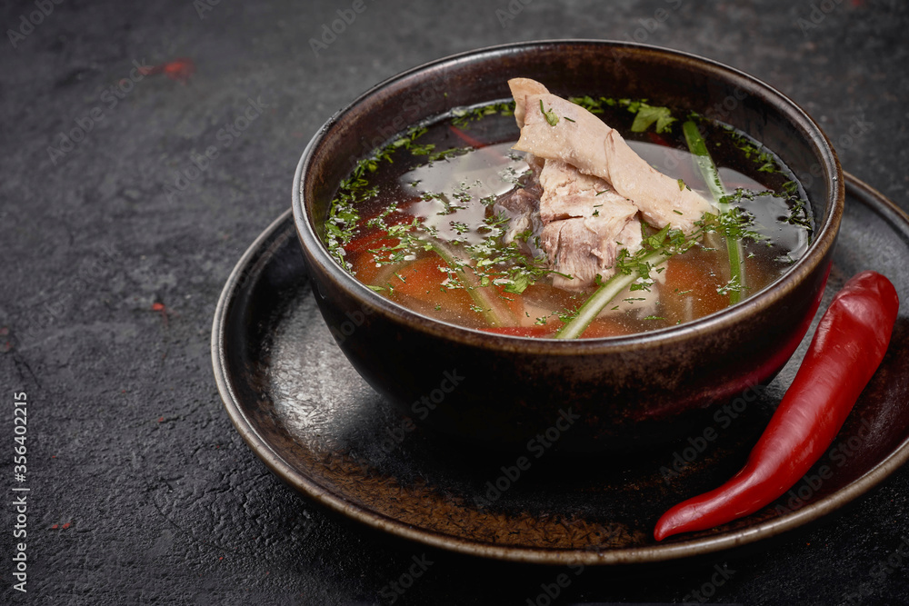 Chicken soup with vegetables in black bowl on black background