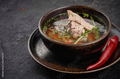 Chicken soup with vegetables in black bowl on black background