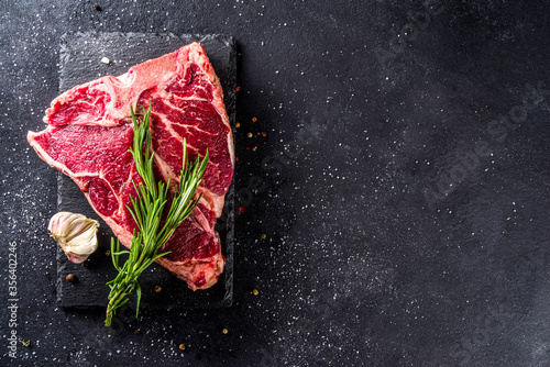 Cooking meat background. Raw aged beef t-bone steak, with spices and herbs for cooking on a gray table background top view photo