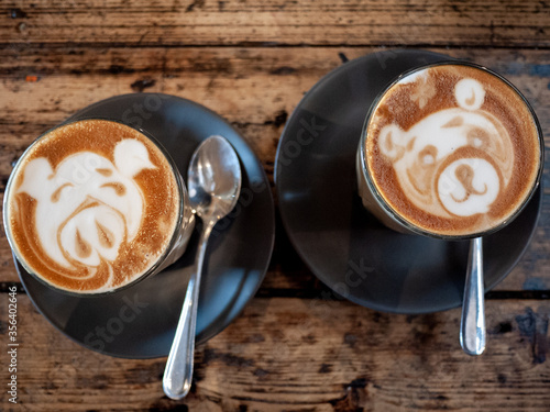 Two cups of coffee with latte art of cute cartoon animal faces on wooden table.