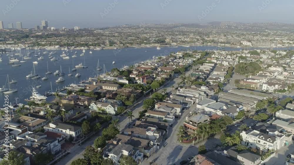 Aerial shot across residential area of Balboa peninsula with boats anchored in Newport harbor and gloomy Corona Del Mar and Fashion Island Mall in the back in Newport Beach, California Aerial shot across residential area of Balboa peninsula with boats anchored in Newport harbor and gloomy Corona Del Mar and Fashion Island Mall in the back in Newport Beach, California