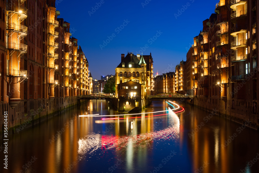 Wasserschloss in Hamburg bei Nacht mit den Lichtspuren eines Schiffes