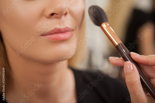 Cropped shot of a woman smiling while makeup artist applying highlighter on her face