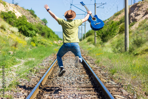 boy with blue guitar jumping on railway