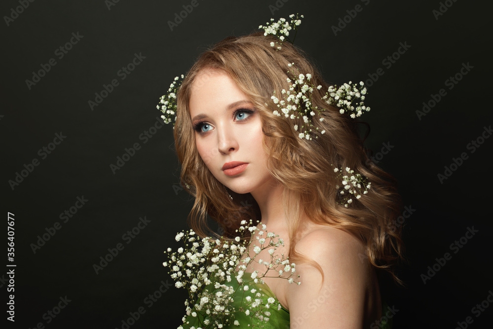 Attractive woman with long healthy curly hair, clear skin and white flowers on black background