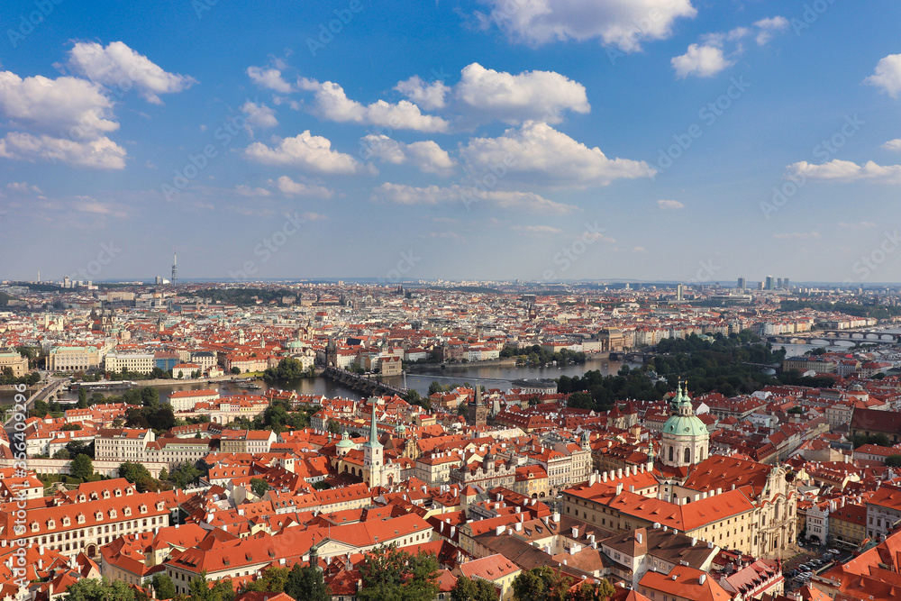 view on the roofs of Prague,  the capital of Czech Republic with cloudy blue sky in summer time from a high point in the middle you can see the Moldova 