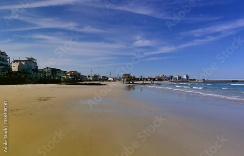 breathtaking view of sunny sandy woljeong beach jeju island South Korea backed by blue sky with reflection on ocean; small city facing seashore separated by a coast road