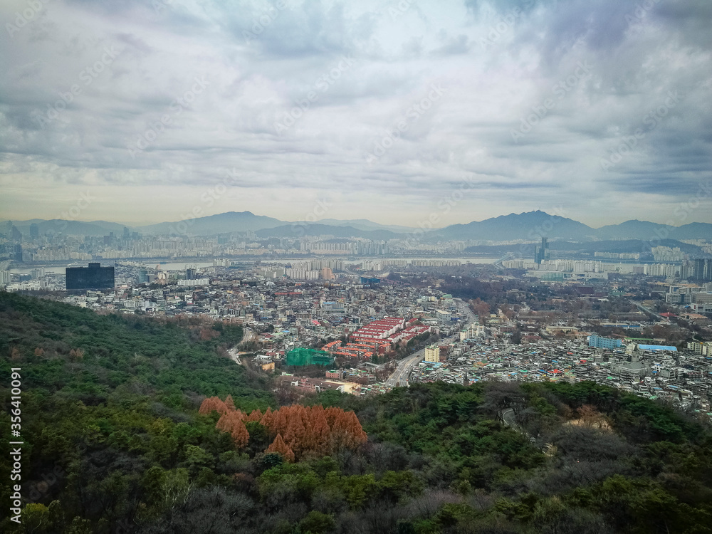 Bird eye view of part of capital city of Seoul from high ground at namsan Seoul South Korea. Visible noise and soft focus due to foggy and cloudy morning. Cloudy blue sky at background.