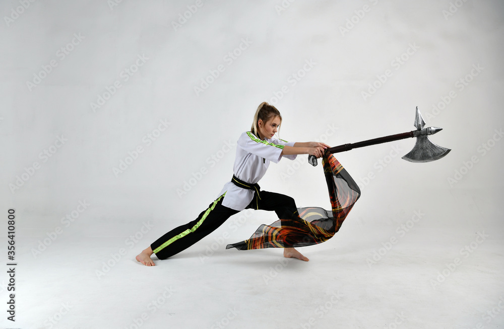 Fototapeta premium beautiful girl in a white-black suit does exercises with a battle ax and a scarf