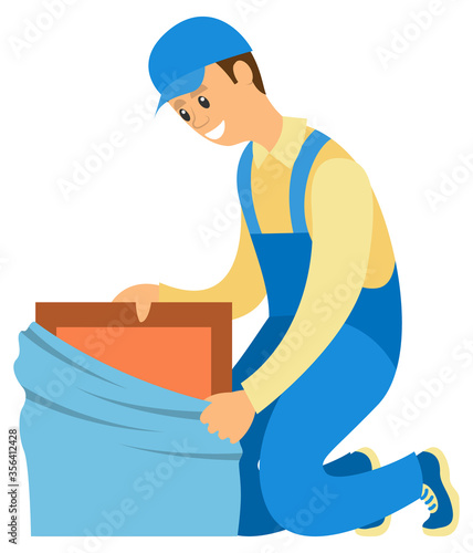 Smiling delivery worker man wearing blue uniform unpacking box isolated on white. Moving house, carton container, furniture banner vector illustration