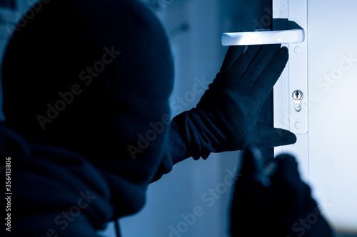 Valokuvatapetti Robber in black balaclava cracking door with metal picklock