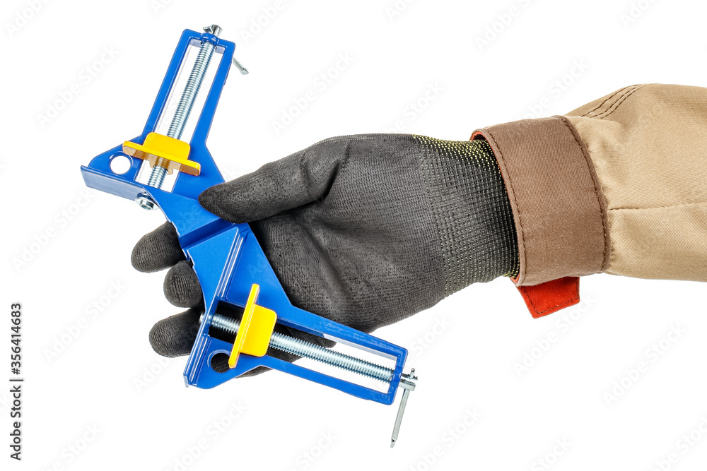 Blue and yellow angle clamp in worker hand in black protective glove and brown uniform isolated on white background Blue and yellow angle clamp in worker hand in black protective glove and brown uniform isolated on white background