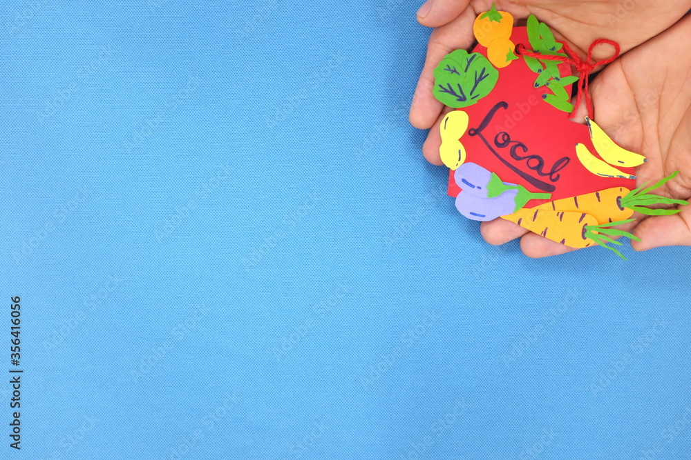 Human hands holding a red heart tag with handwritten word local and vegetables. Support, promote, buy, shop and love local farmers market produce concept. Blue background, top view, with copy space.