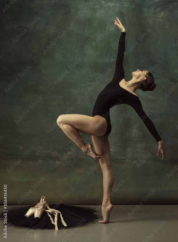 Confident. Graceful classic ballerina dancing, posing isolated on dark studio background. Elegance black tutu. Grace, movement, action and motion concept. Looks weightless, flexible. Fashionable.