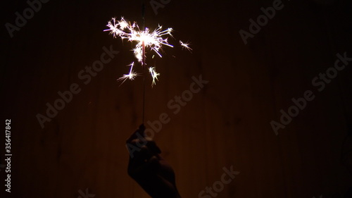 A woman holds a Bengal fire in her hand. Sparklers shine in the dark. Hand with a sparkler closeup