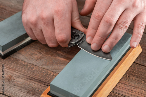 Tablou pe pânză Man sharpening a pocket knife using a whetstone