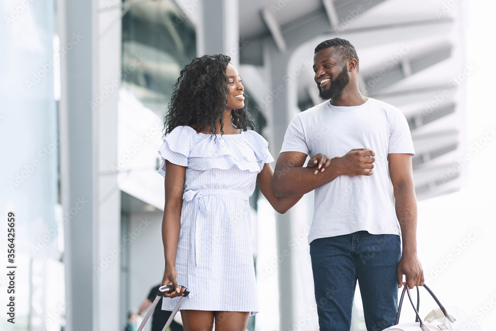 Obraz premium Romantic Travel. Happy Black Couple Walking Near Airport Building With Luggage