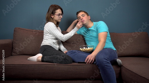 A woman feeds a man popcorn. The girl puts popcorn in the man's mouth. A couple is watching TV. Sitting on the couch