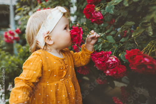 Child girl smelling flowers red roses in garden childhood baby summer lifestyle aromatherapy harmony with nature