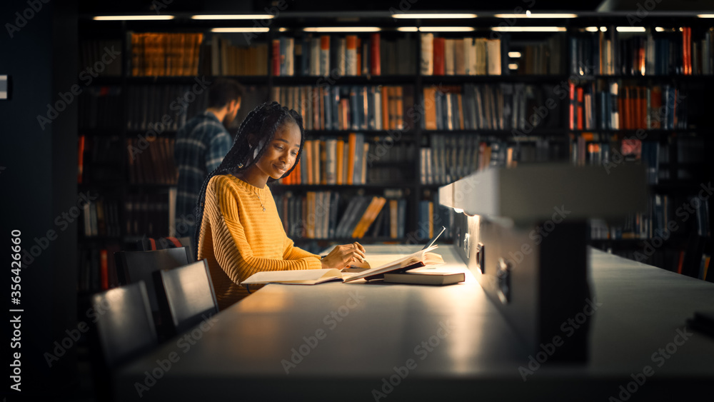 University Library: Gifted Black Girl uses Laptop, Writes Notes for the Paper, Essay, Study for Class Assignment. Students Learning, Studying for Exams College. Side View Portrait with Bookshelves - obrazy, fototapety, plakaty 