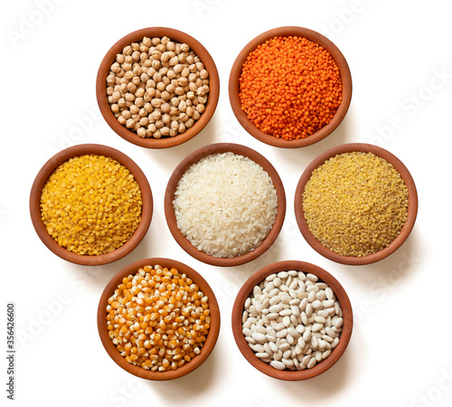 Dry legumes in arranged ceramic bowls Yellow lentils, dry chickpeas, Red lentils, white rice, dry beans, corn seeds, bulgur wheat. Isolated top view.