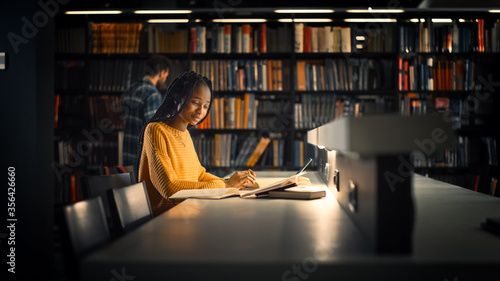 Fotografija University Library: Gifted Black Girl uses Laptop, Writes Notes for the Paper, Essay, Study for Class Assignment