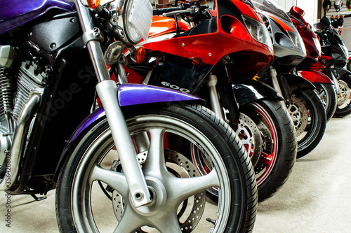 Beautiful group parking of motorcycles in a showroom for sale, in a store close-up. Maintenance of sportbikes, road bikes in the workshop. Moto parts, wheels, headlights, engine. © Maksim