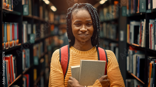 University Library Study: Portrait of a Smart Beautiful Black Girl Holding Study Text Books Smiling Looking at the Camera. Authentic Student Does Research for Class Assignment, Exams Preparationtion