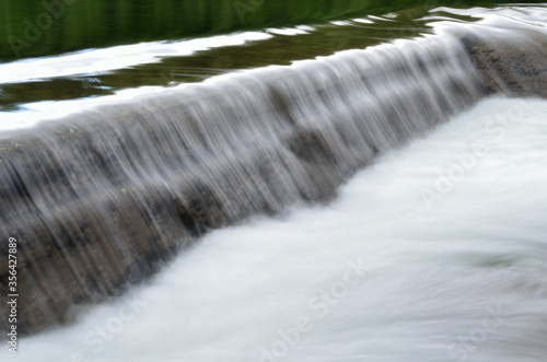 milky white river flood torrent over concrete barrier in summer  long exposure