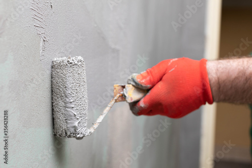 A close-up view of an experienced construction worker applying damp insulation using a paint roller on a wall.