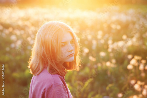 beautiful teenager girl on background dandelions meadow at sunset