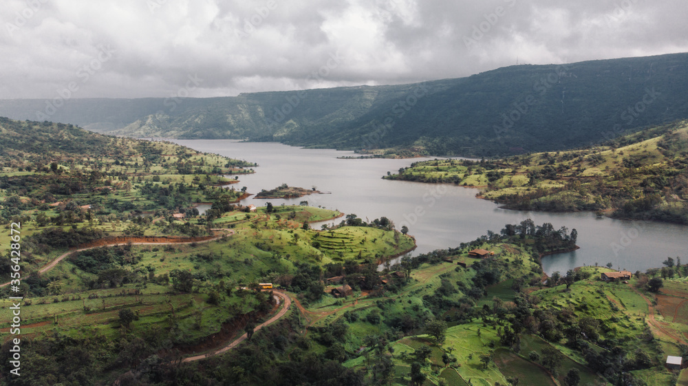 Obraz premium Aerial/Drone View of a river valley and an offbeat holiday resort in green surroundings during Monsoon season in Maharashtra, India.