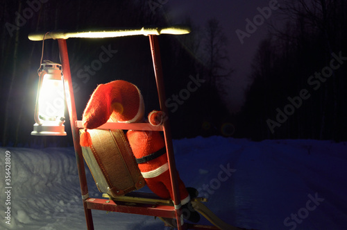 small santa travelling home on kicksled on snowy road with suitcase and lantern photo