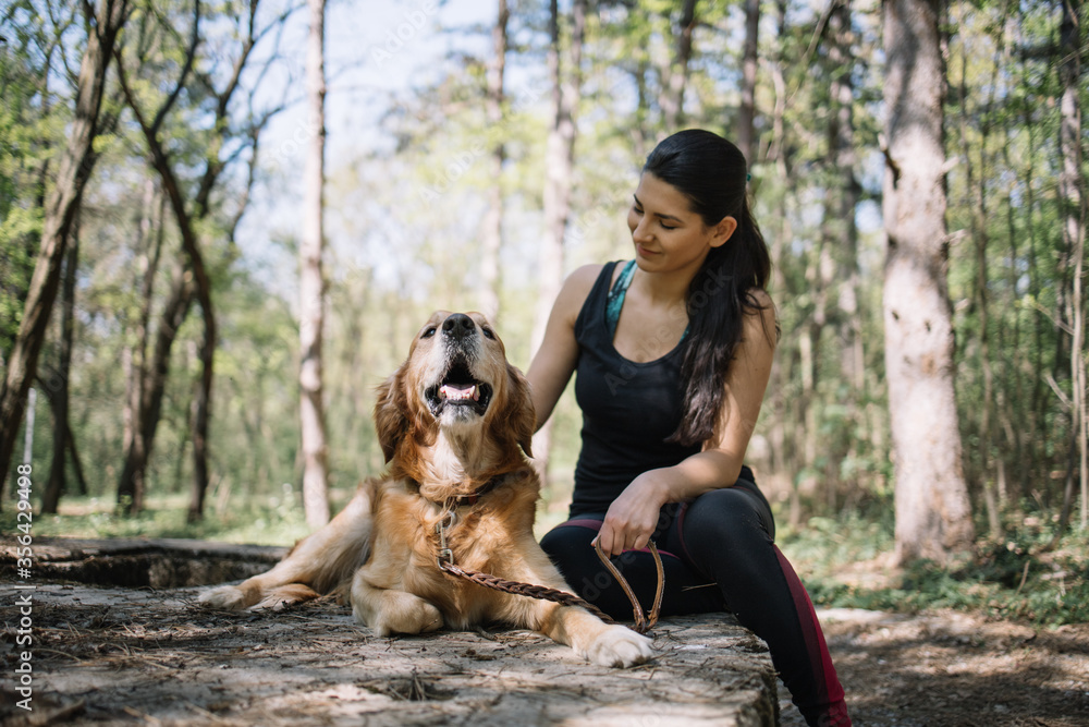 Happy girl sitting next to her dog in nature. Smiling girl in sportswear resting in forest with her dog in sunny day. Happy girl sitting next to her dog in nature. Smiling girl in sportswear resting in forest with her dog in sunny day.