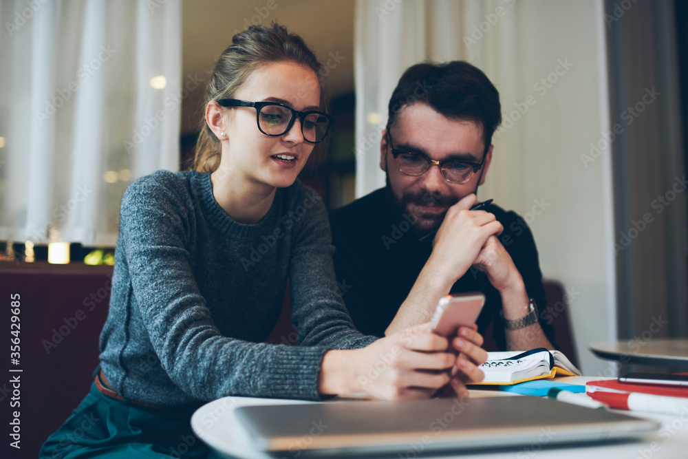 Hipster girl holding book while guy sitting near with smartphone in hand