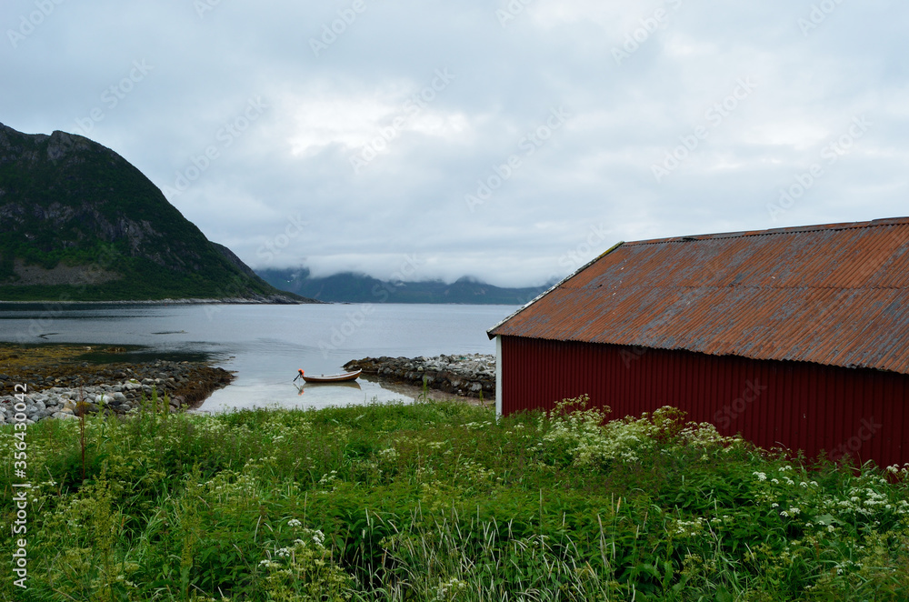 old red boat house with cloudy mountain range background and small docked boat