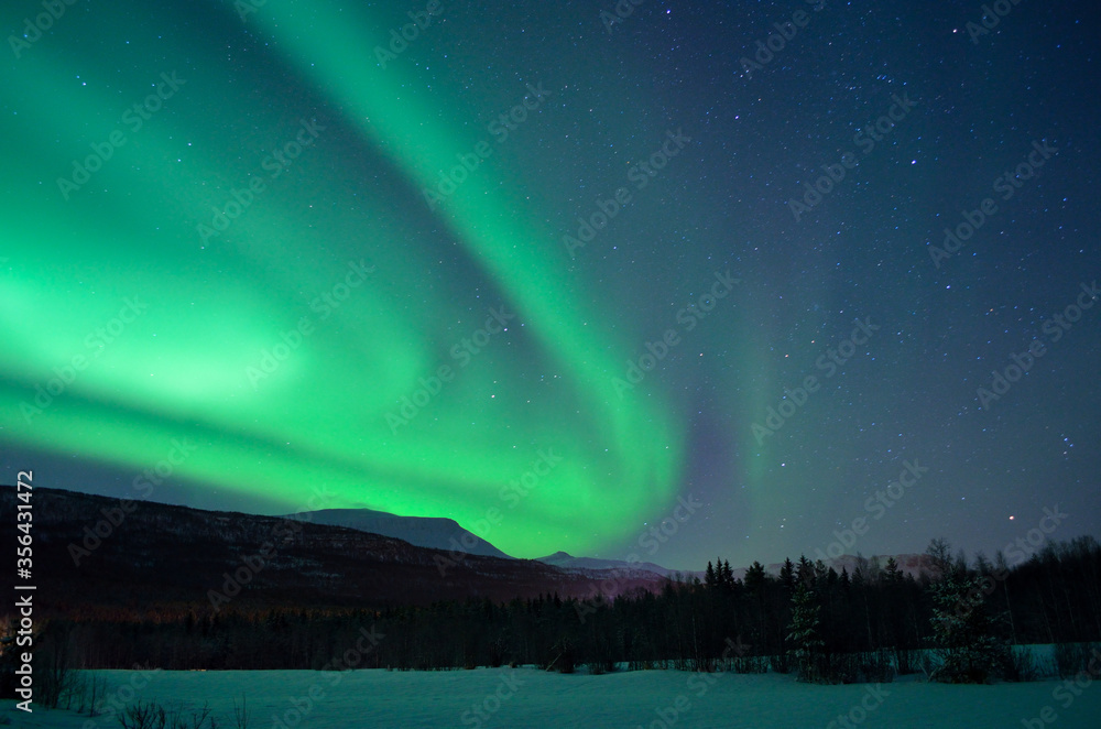 strong aurora borealis dancing over snowy field and mountain in the arctic circle