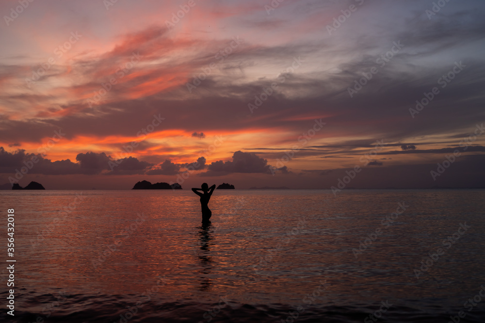 Silhouette of a woman in the water of sea or ocean at sunset.