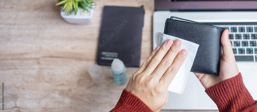 Woman cleaning money wallet and gadgets by wet wipes tissue and alcohol disinfectant on workplace during work at home, protection coronavirus (Covid-19) infection. New Normal and Clean surface concept