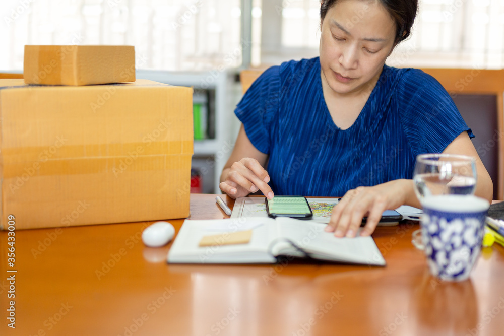 Woman checking order in cell phone online shopping store for delivery package to customer from home office. Woman checking order in cell phone online shopping store for delivery package to customer from home office.