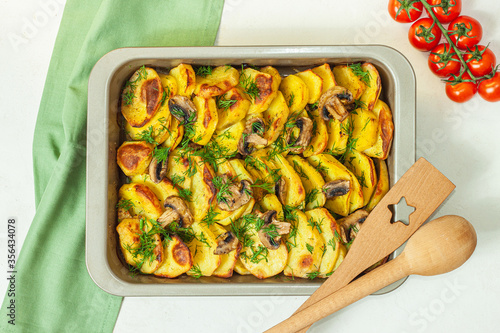 Potato wedges baked with mushrooms, herb oven roasted, with thyme, a close-up in a baking tray photo