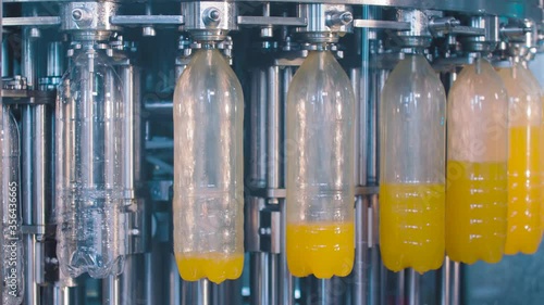 Transparent plastic bottles move on conveyor belt and filled of juice 