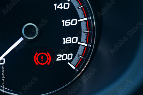 the screen of black car's gauge with white number of speed level and red warning sign of handbrake